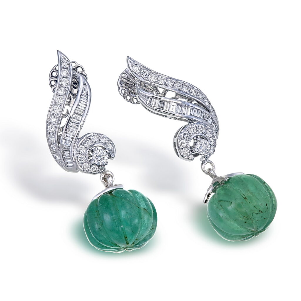 Pair of elegant white gold drop earrings featuring carved green emeralds and diamond-encrusted swirling designs.